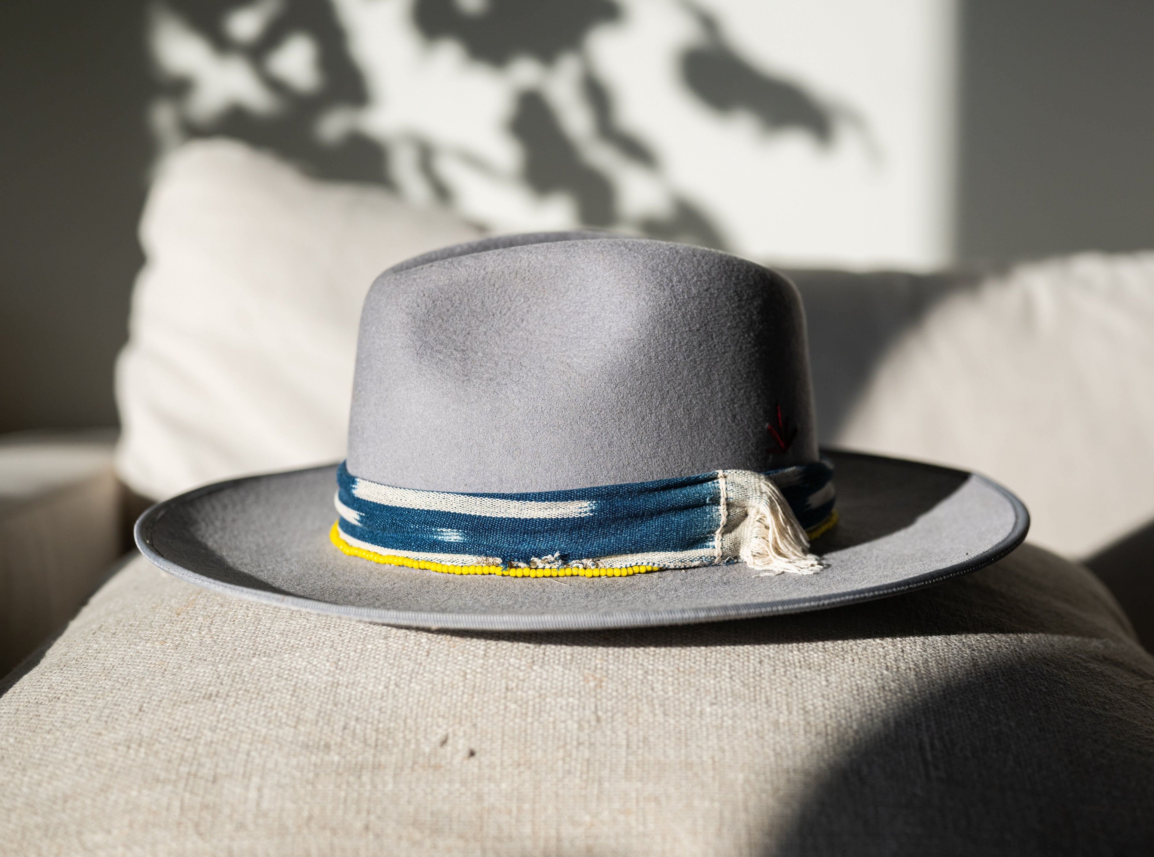 Agave Blossom gray felt hat with blue ikat band and gold beading, styled on linen.