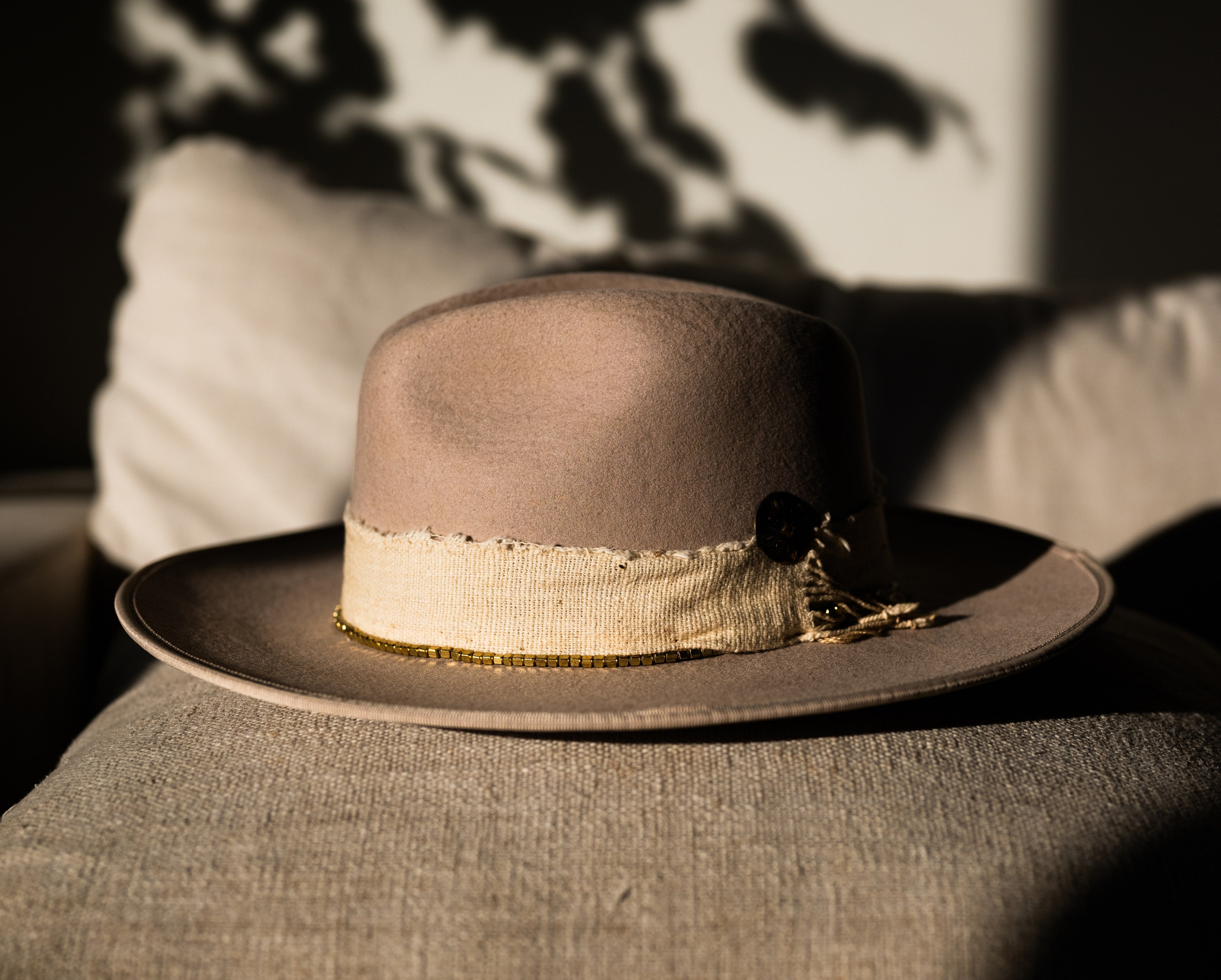 Colorado Summer camel felt hat with frayed ivory band, on linen in dappled shade.
