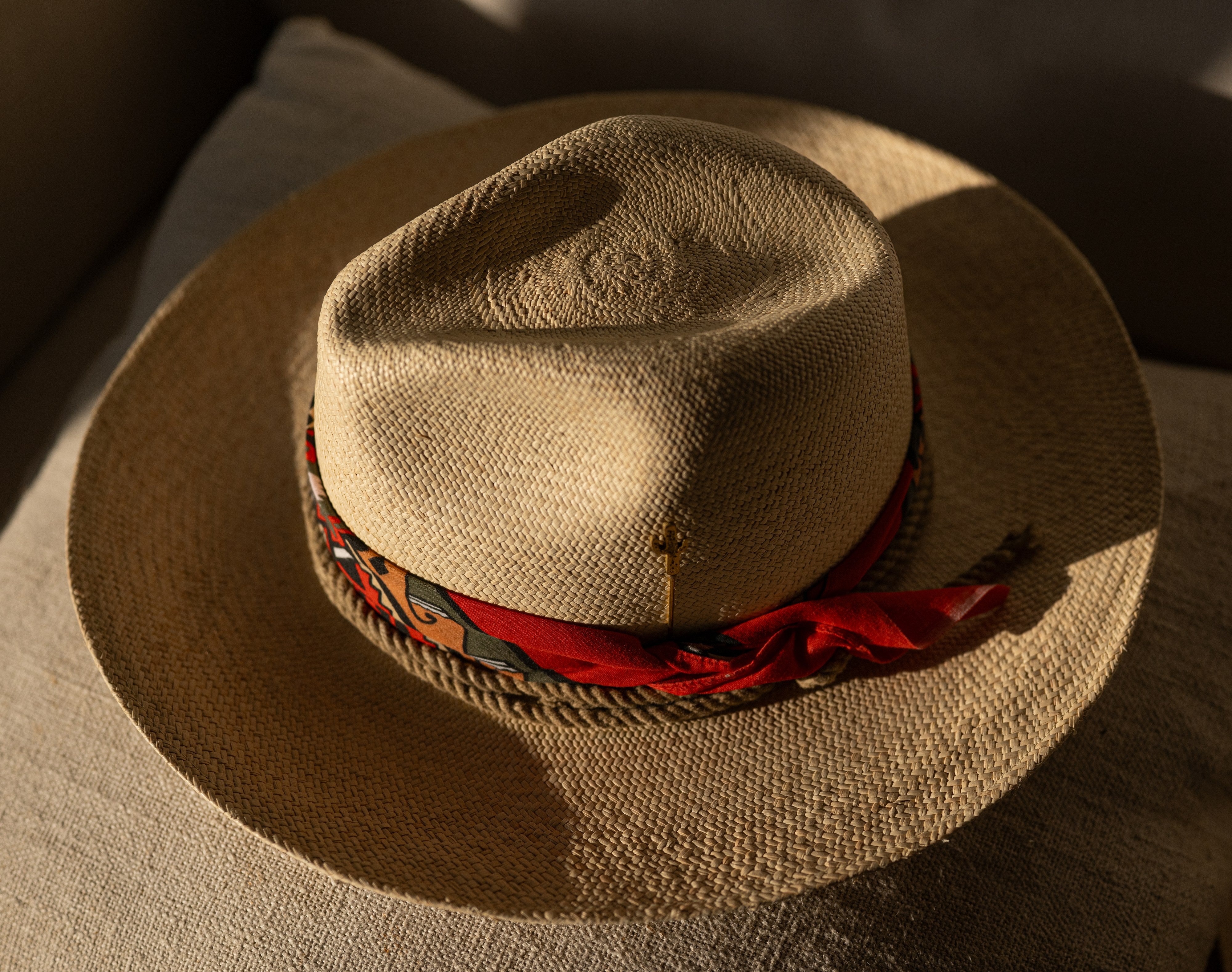 Firebird straw hat with red printed silk scarf band, viewed from above on linen.
