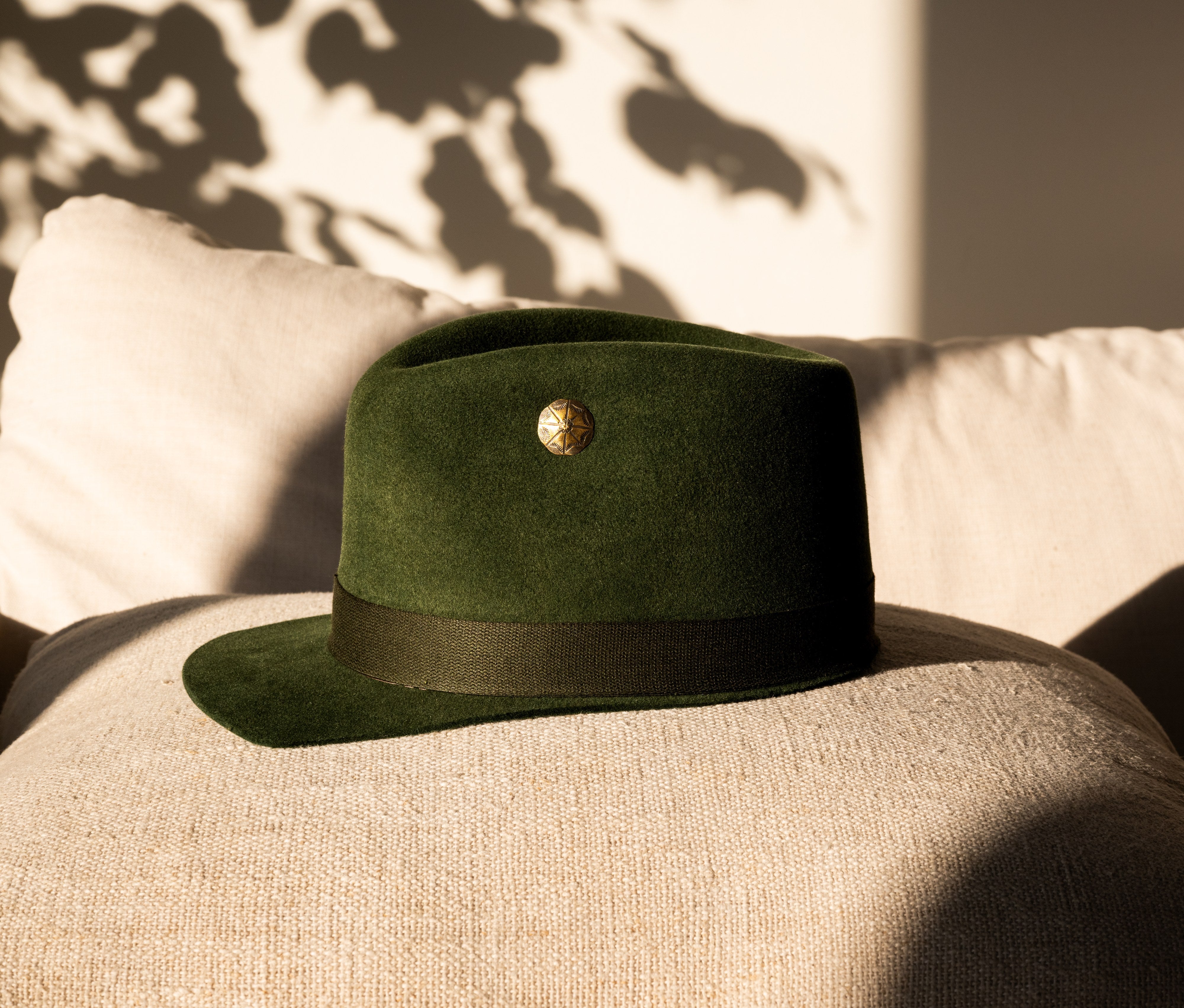Hilltop olive green low-crown hat photographed against a sunlit interior wall.