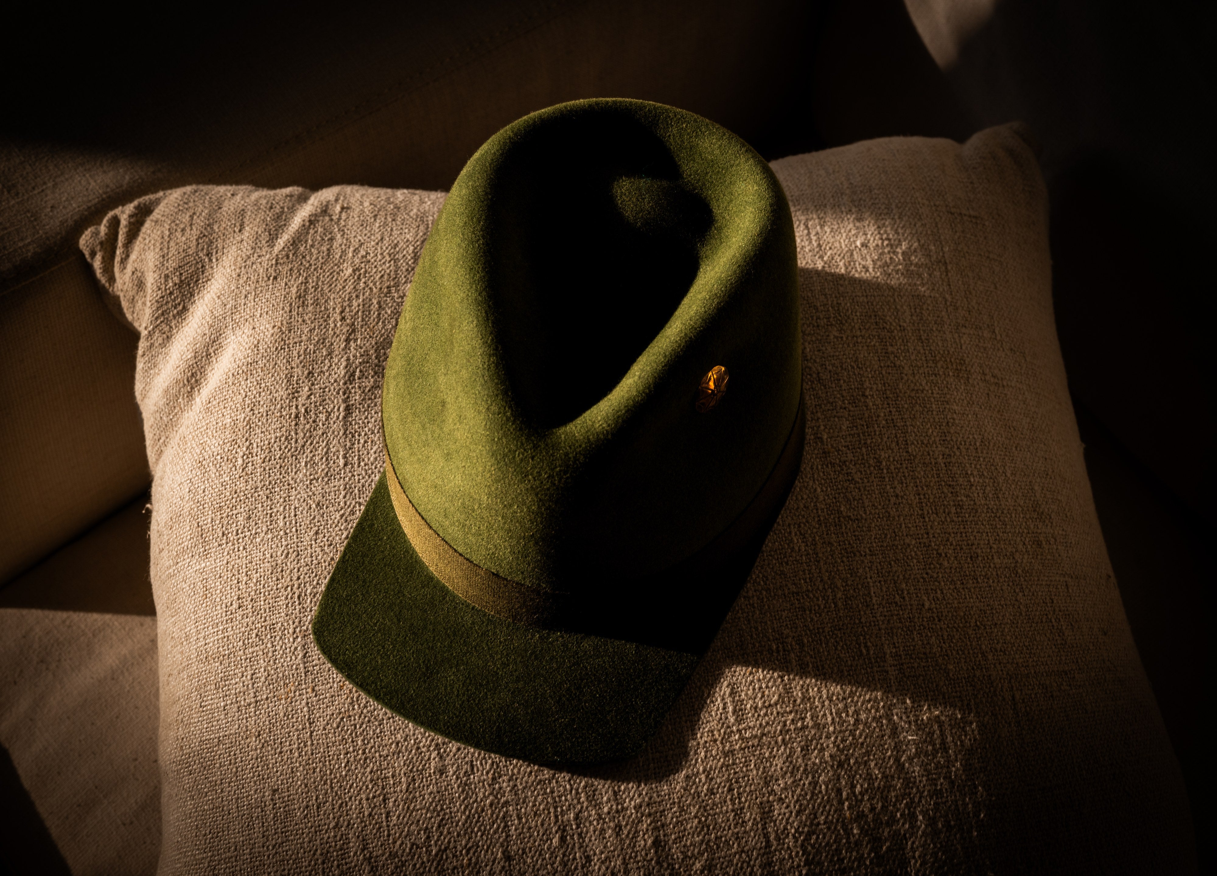 Hilltop olive green hat resting crown-down on a linen cushion, brim curl visible.
