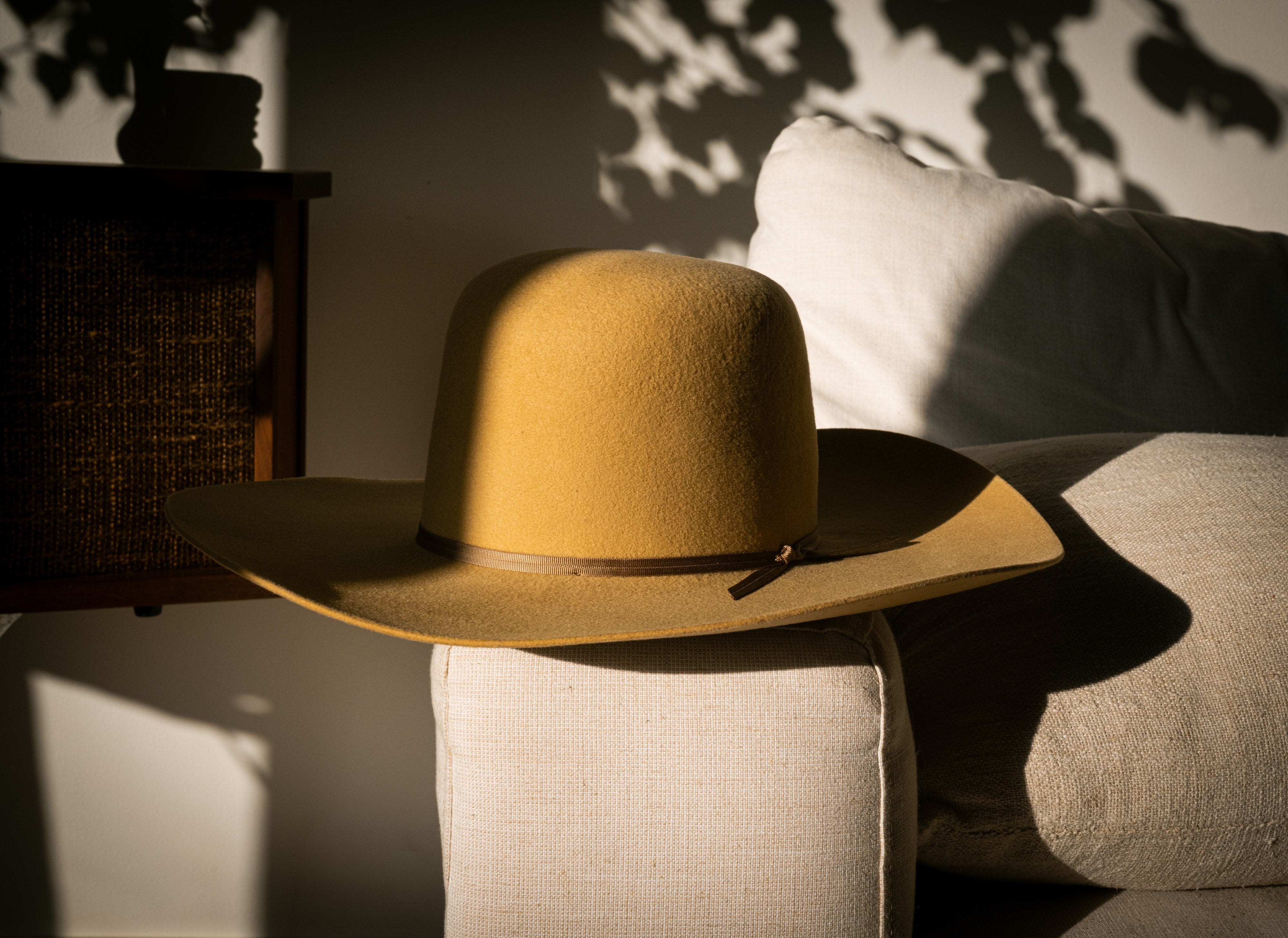 Honey Hour camel open-crown hat with leather tie band, resting on linen in afternoon light.