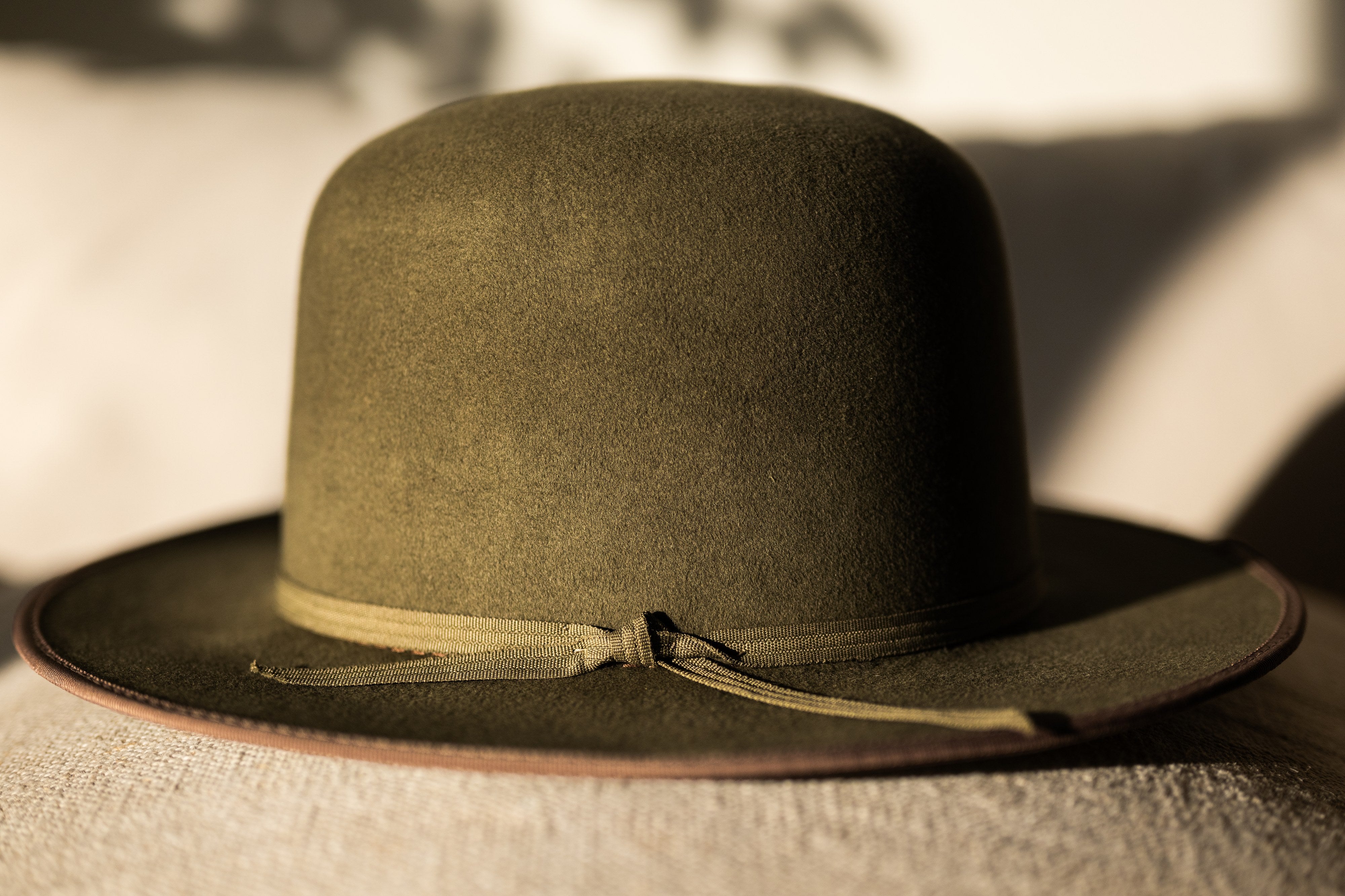Sweet Grass olive fur-felt hat with self-tie band, close on linen in golden light.